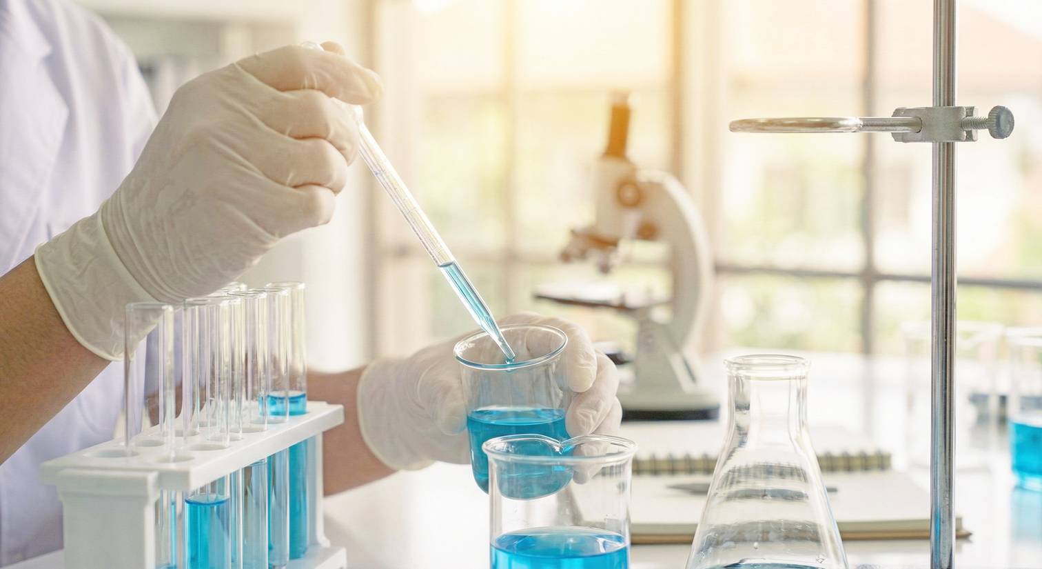 An image of a gloved hand and lab equipment with blue liquid